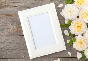 Blank photo frame and white roses over wooden table background