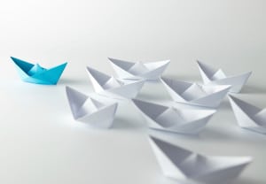 Leadership concept with blue paper ship leading among white