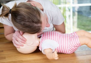Woman performing CPR on baby training doll, checking for signs of breathing