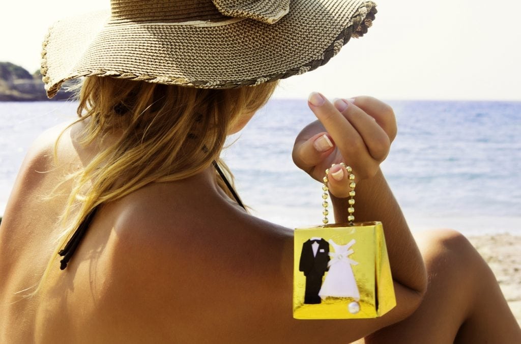 Young woman holding gift box of bride and groom and watching sea on the beach