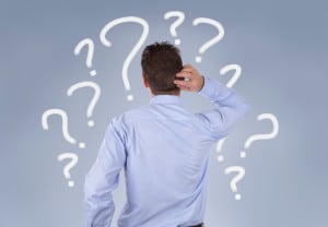 Confused businessman standing in front of a wall of question marks